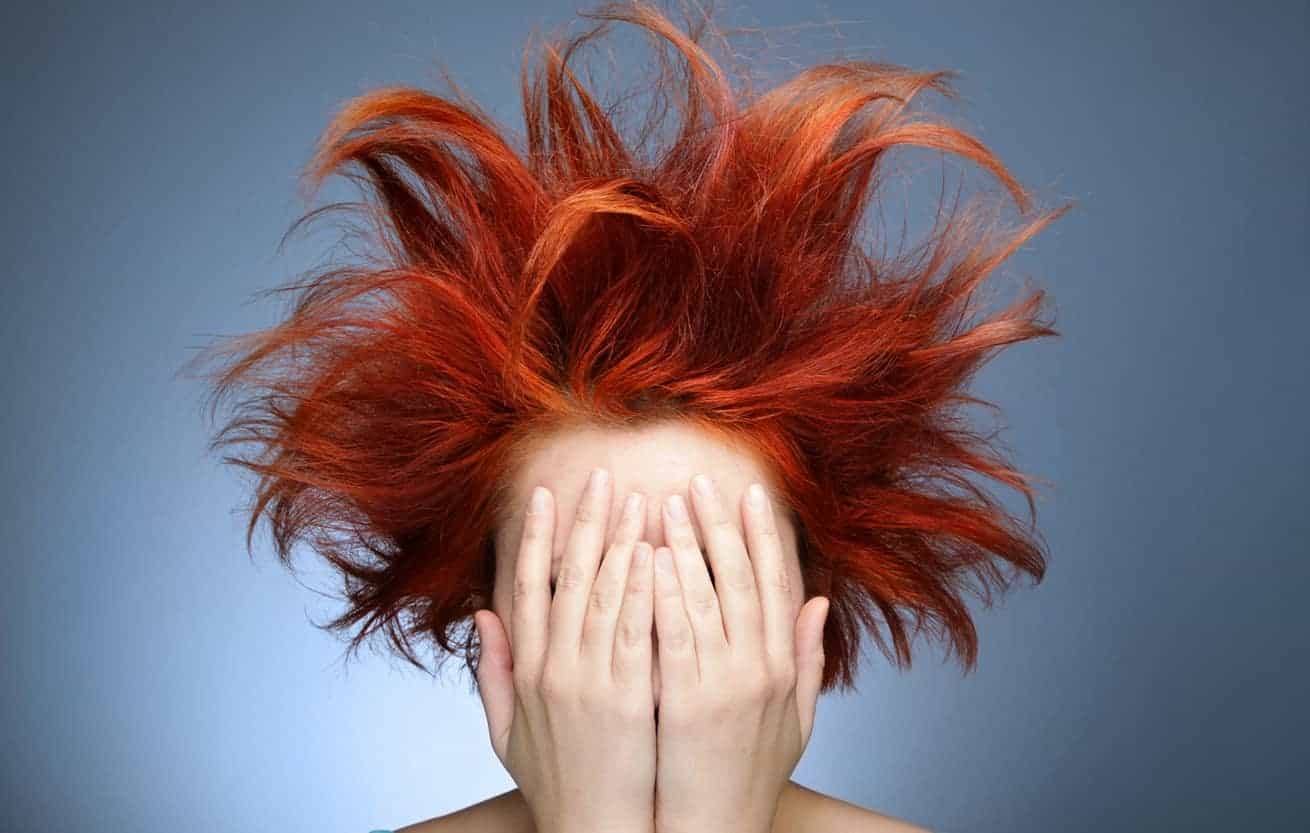 Vrouw met wild rood pluizend haar houdt haar handen voor haar gezicht