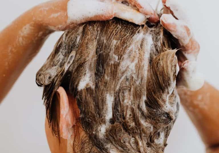 Persoon wast het haar onder de douche in met shampoo