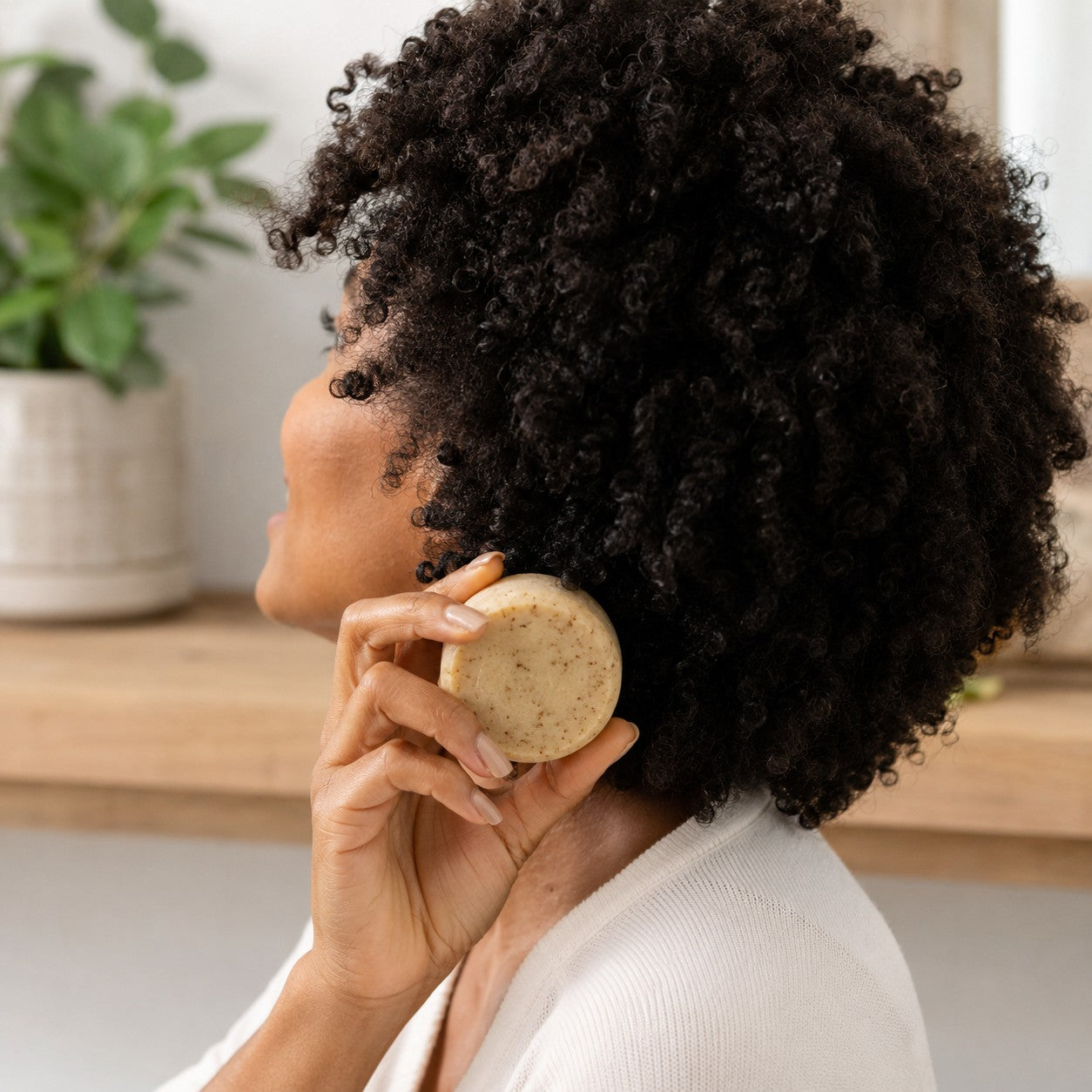 Vrouw met kroeshaar houdt een ronde shampoo bar naast haar hoofd